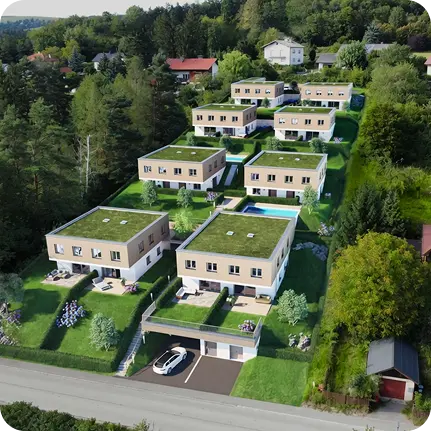 Vogelperspektive einer Neubausiedlung mit mehreren modernen Häusern mit Begrünung auf den Flachdächern an einem bewaldeten Hang.